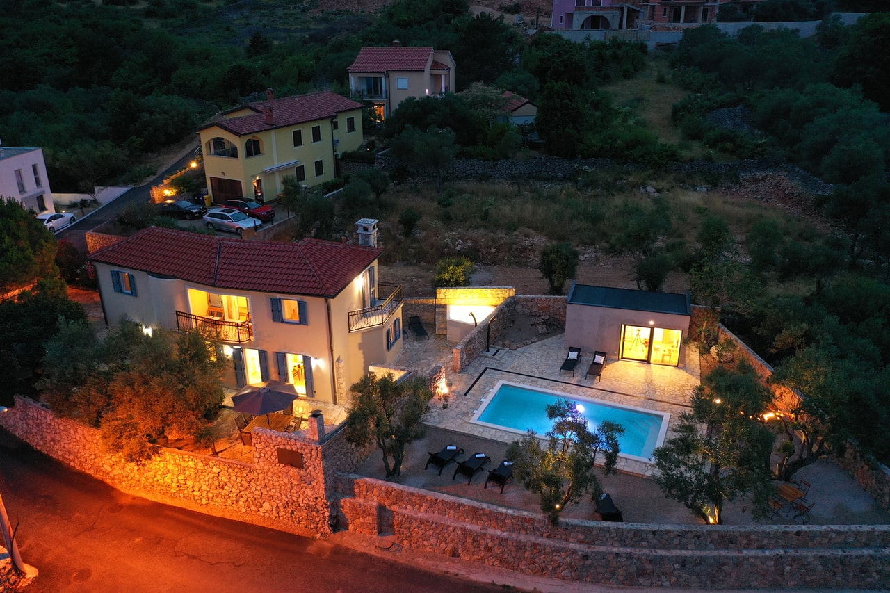 Villa Pinia in Vrbnik with an illuminated private pool and separate pool house at dusk